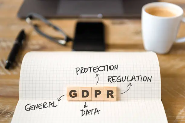 Closeup on notebook over wood table background, focus on wooden blocks with letters making GDPR General Data Protection Regulation text. Business concept image.