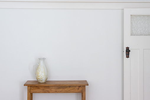 White jug on wooden side table against wall with retro doorf