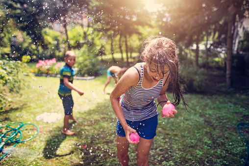 Little boy is throwing water balloons his sister. The girl is running for cover holding two water balloons
Nikon D810