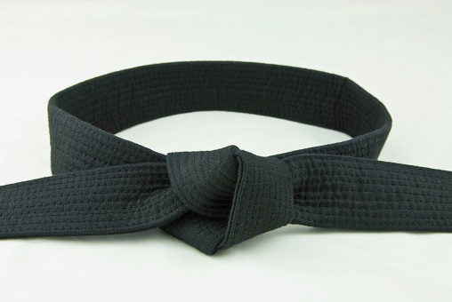 Beautifully knotted old shabby black belt of a martial artist on a dark background.