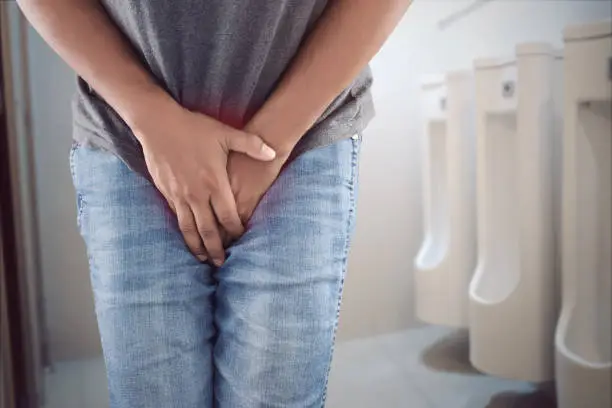 Photo of Asian man wants to pee and is holding his bladder.