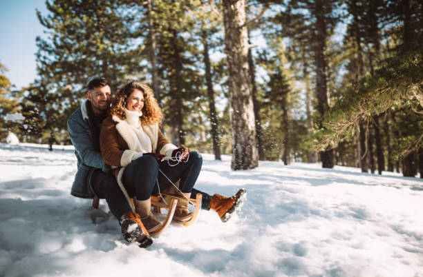 joven pareja en vacaciones de navidad, montar en trineo en la nieve - deslizarse en trineo fotografías e imágenes de stock