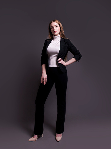Intelligent young caucasian businesswoman wearing trendy smart casual clothes looking fresh beautiful confident successful with professional natural make-up and hairstyle long straight brown red hair Fashion model full length body studio portrait on dark gray background