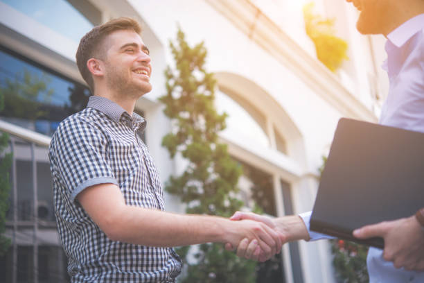 istock Two happy young men shaking hands with town building background 962790136