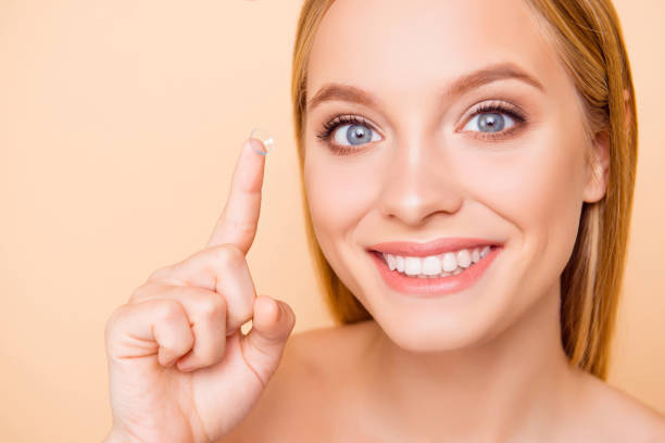 close up portrait of pretty, charming, cute, cheerful, positive, glad, nude, natural girl with beaming smile gesturing crystalline lens on forefinger, isolated on beige background - human eye eyesight optometrist lens imagens e fotografias de stock