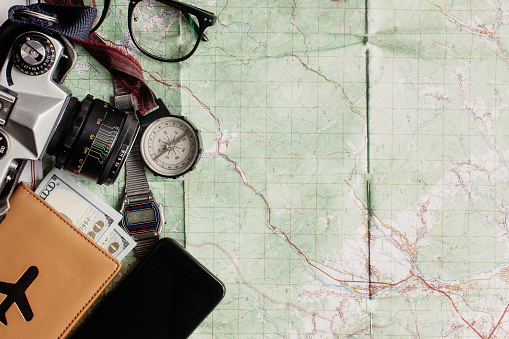 wanderlust and adventure concept, old compass phone photo camera glasses passport and money lying on map, top view, space for text, vintage toned image