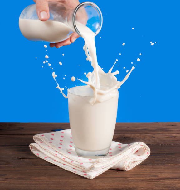 istock Milk from a jug pouring into glass on a blue background 962817732