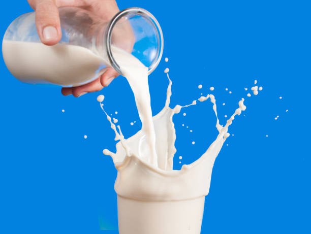 istock Milk from a jug pouring into glass on a blue background 962822296
