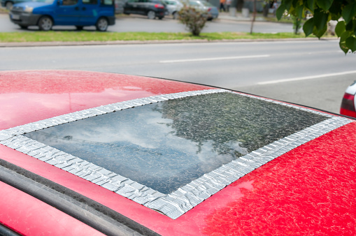 Dañado, ventana de techo de cristal o en el techo en el coche rojo pegado con cinta adhesiva para evitar que el agua para venir en el interior del vehículo photo