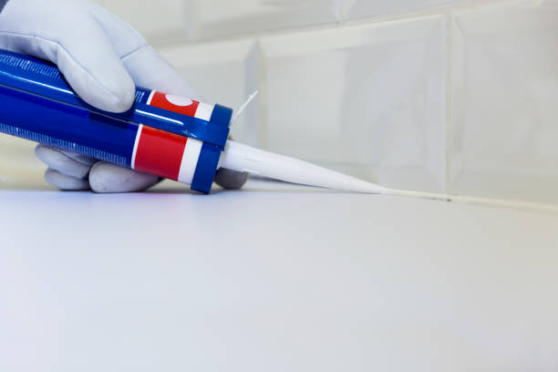 Plumber applying silicone sealant to the countertop and ceramic tile. Home improvement, kitchen renovation concept stock photo