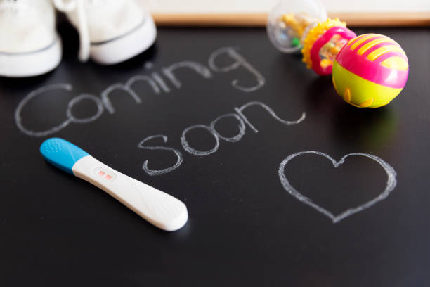 Waiting for labour, maternity concept. "Coming soon" words on black chalkboard with positive pregnancy test, white baby shoes and rattle stock photo