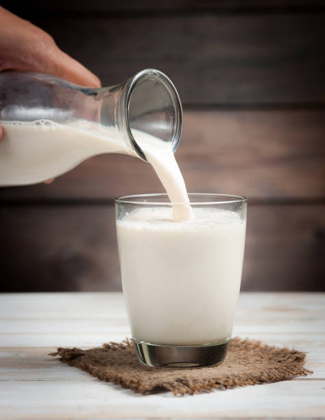 istock Milk from a jug pouring into glass on wooden 962832802