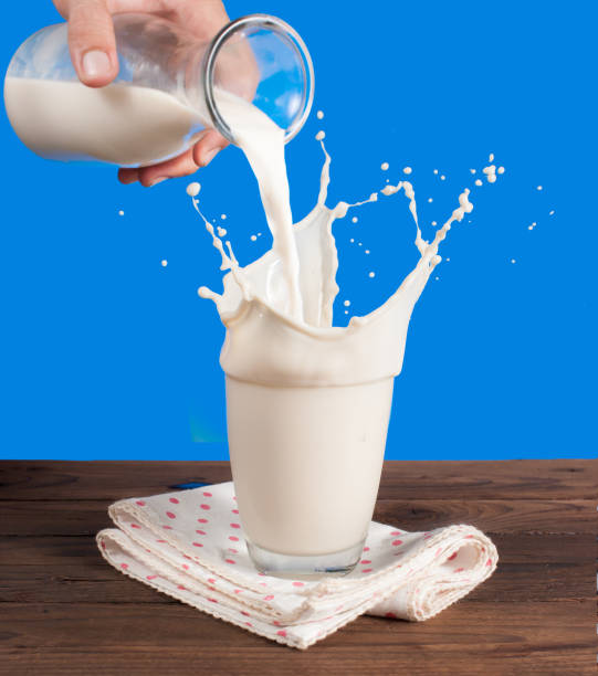 istock Milk from a jug pouring into glass on a blue background 962836652