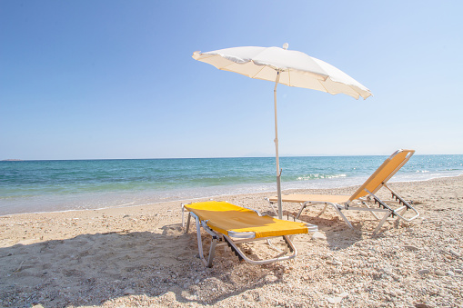 Two yellow sun beds and white beach umbrella on a sandy sea beach on a sunny summer day. Summer vacation concept.