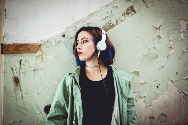 Male punk person with yellow and red Mohawk hairstyle, listening music on headphones, standing on the street in city.