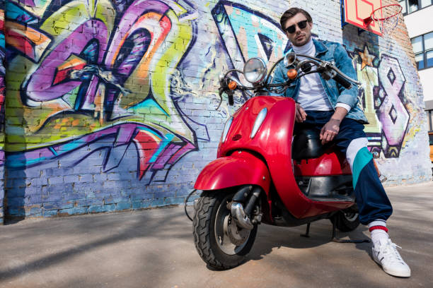 istock handsome young man on vintage red scooter looking at camera in front of brick wall with graffiti 962853148