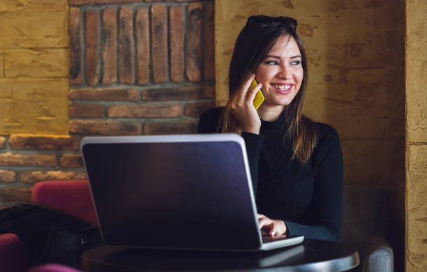 istock Woman  sitting in cafe using her laptop and talking on mobile phone. 962860182