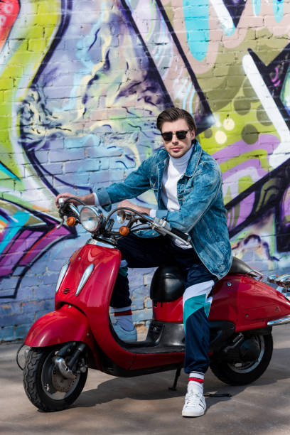 istock attractive young man on vintage red scooter in front of brick wall with graffiti 962861172