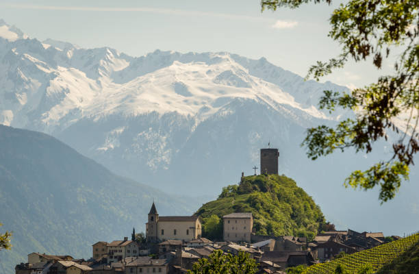 A small village in Switzerland with a castle and a church on a hill overlooking the snow capped peaks and glaciers.