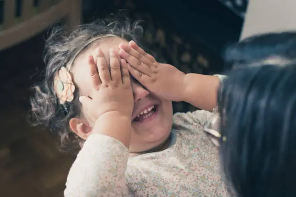 Happy little girl playing peekaboo game with mother and covering her eyes with hands.