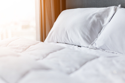 Bed maid-up with clean white pillows and bed sheets in beauty room. Close-up. Lens flair in sunlight.