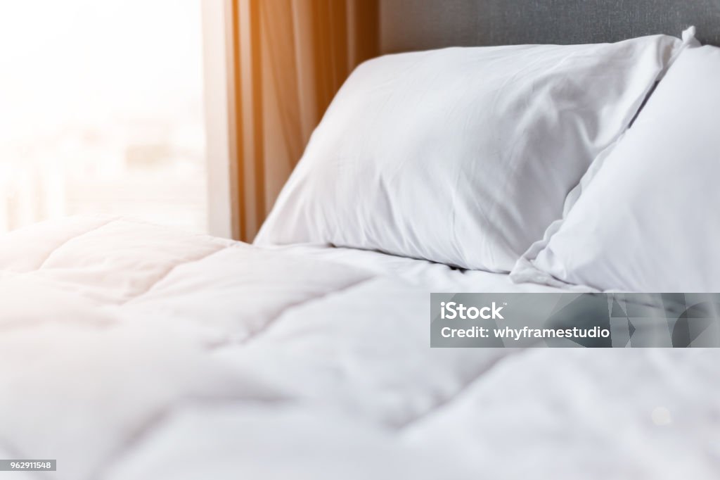 Bed maid-up with clean white pillows and bed sheets in beauty room. Close-up. Lens flair in sunlight. Bed - Furniture Stock Photo