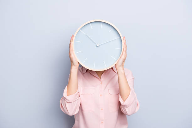 it's 10:10 o'clock. portrait of charming pretty positive cheerful woman closing covering head face with round clock isolated on grey background - timing is everything imagens e fotografias de stock