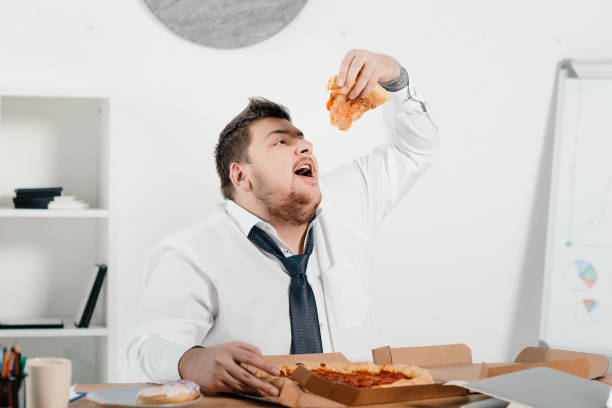 istock overweight businessman eating pizza for lunch at workplace 962916176