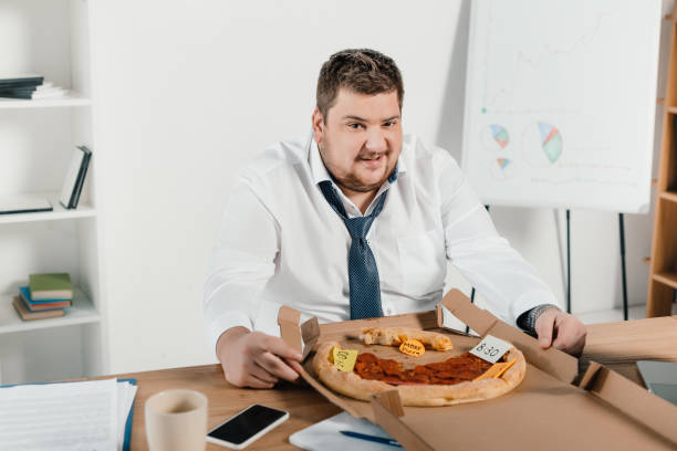 istock overweight businessman eating pizza at workplace in office 962916392
