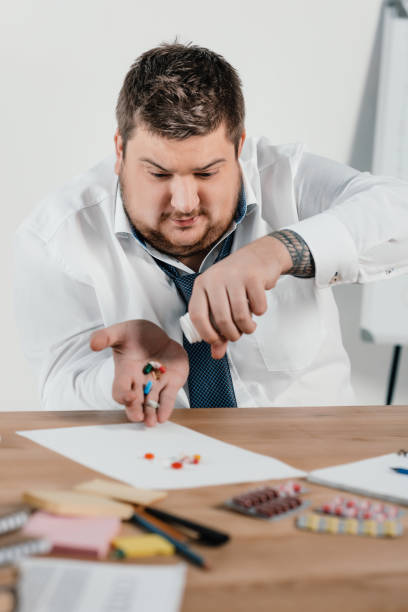 istock fat businessman with pills sitting at workplace in office 962920934