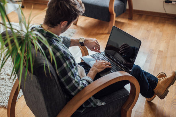 istock Man using laptop at home and checking the time on his watch 962926090