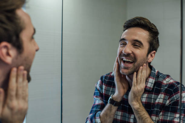 Satisfied man looking at his beard in the mirror reflection at bathroom Man checking his mirror image in the toilet at home vanity mirror stock pictures, royalty-free photos & images