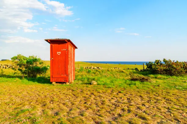 Lovely little red outhouse on a coastal meadow on a sunny day.