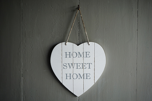 Home sweet home door sign, hanging on a wooden door by a rope. A welcoming message is in contrast with the gray background.