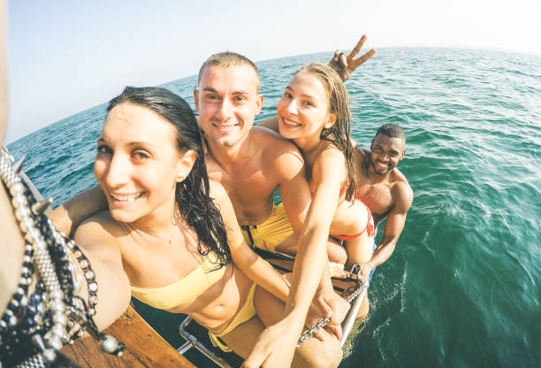 young multiethnic friends taking selfie after swimming on sailing boat sea trip - rich happy guys and girls having fun in summer party day - exclusive vacation concept - bright warm  vintage filter - beach nautical vessel party clothing imagens e fotografias de stock