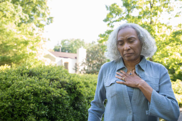 Chest Pains A senior woman makes a pained expression and grabs her chest.  She is outdoors.  She is African ethnicity, has gray hair, and it wearing a blue shirt. heart internal organ photos stock pictures, royalty-free photos & images