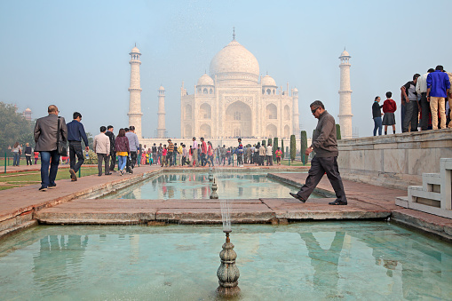Agra, India - November 29, 2015: Famous Taj Mahal with visiting tourists - an immense mausoleum of white marble built by the Mughal emperor Shah Jahan in memory of his favorite wife Mumtaz Mahal.