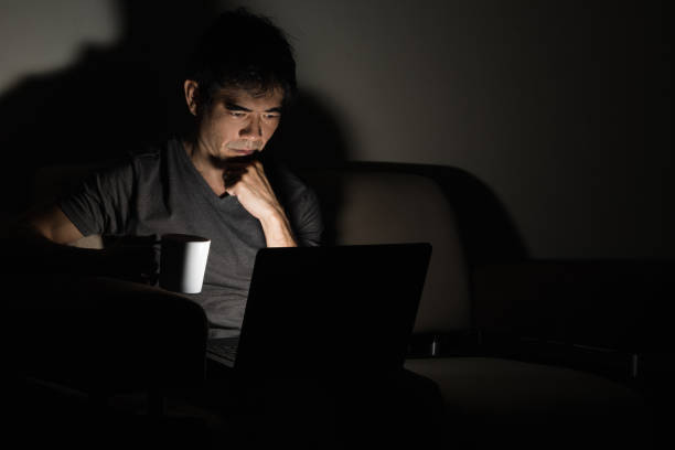 istock Asian man working on laptop from home at night, sitting relaxed on couch 962959586