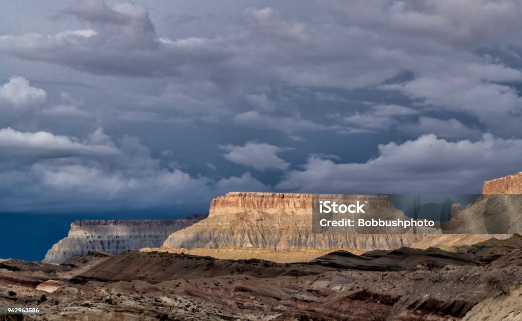 Buttes in Cainesville Badlands near Capital Reef National Park The sun lights up buttes in the Cainesville Badlands near Capital Reef National Park, with dark stormy clouds in the background Bears Ears National Monument Stock Photo