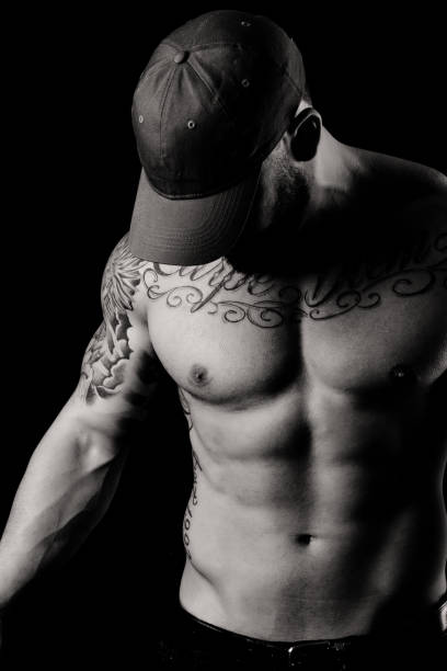 Muscular Shirtless Man In Studio A 26 year old, muscular bodybuilder in studio against a plain black background highlighting abdominal muscles. chest tattoo men stock pictures, royalty-free photos & images