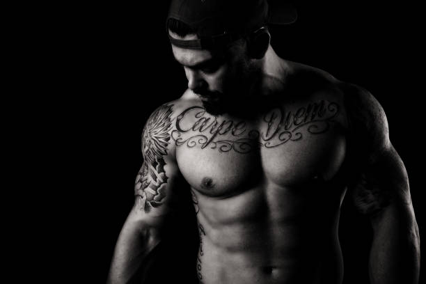 Muscular Shirtless Man In Studio A 26 year old, muscular bodybuilder in studio against a plain black background highlighting abdominal muscles wear his cap backwards. chest tattoo men stock pictures, royalty-free photos & images