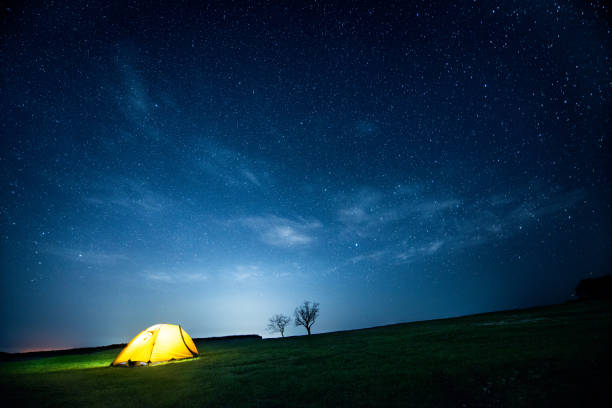 Glowing camping tent in the night mountains under a starry sky