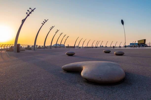 Seating and lights on the promenade in Blackpool, Lancashire. With curved street lamps and round benches for sitting.\n\n+ the structures in this photo are not sculptures, they are street furniture found across the seafront in Blackpool. The tall curved items are street lights and the rounded blocks are public benches for sitting.