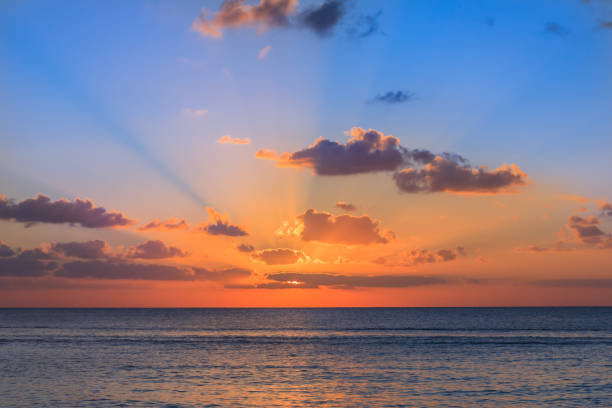 Sunset on the Caribbean sea. The sunset photo has been taken from island Cozumel - Mexico. The sky is blue with a yellow - purple sun on the horizon. Sun rays of light escaping through the clouds.