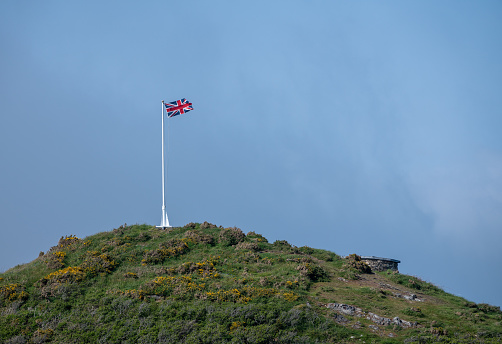 Union Jack flag on flagpole on hilltop cliff with blue sky in background