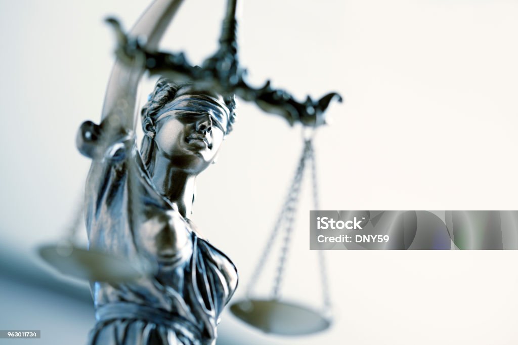 Statue Of Lady Justice In Front Light Colored Background A close up and a low angle view of a statue of lady justice.  The image is photographed with a very shallow depth of field with the focus being on her face. Lady Justice Stock Photo