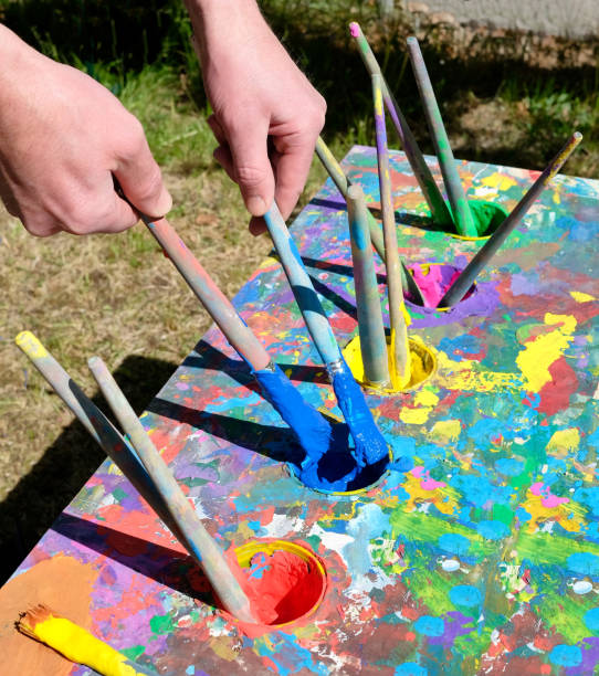 istock Male hands holding loading brushes with blue paint from ouache paint table 963030932