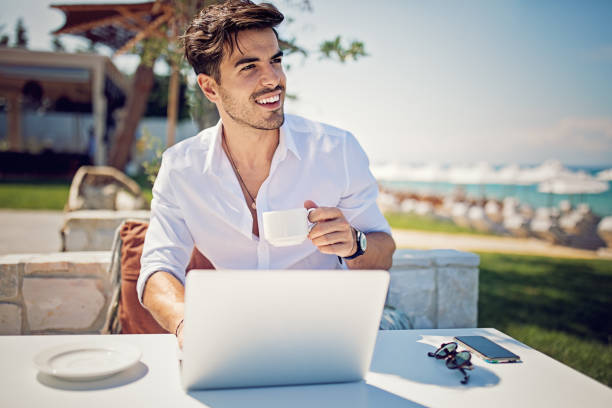 young businessman is working and drinking coffee on the beach - on beach laptop working imagens e fotografias de stock