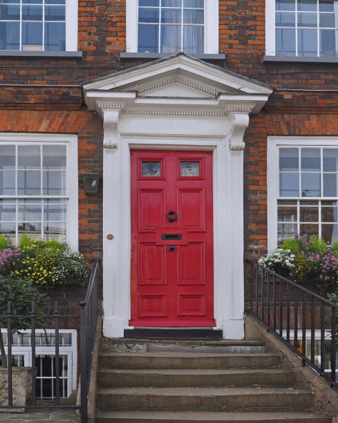 Close up color image depicting the exterior of a building on a traditional city street in Notting Hill, London, UK. The house has a pretty red door, blue walls, and the facade is decorated with a freshly blooming rose bush. Room for copy space.