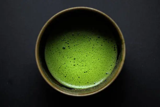 Usucha (conventional matcha) in a yellow-rimmed black bowl on a black slate background.